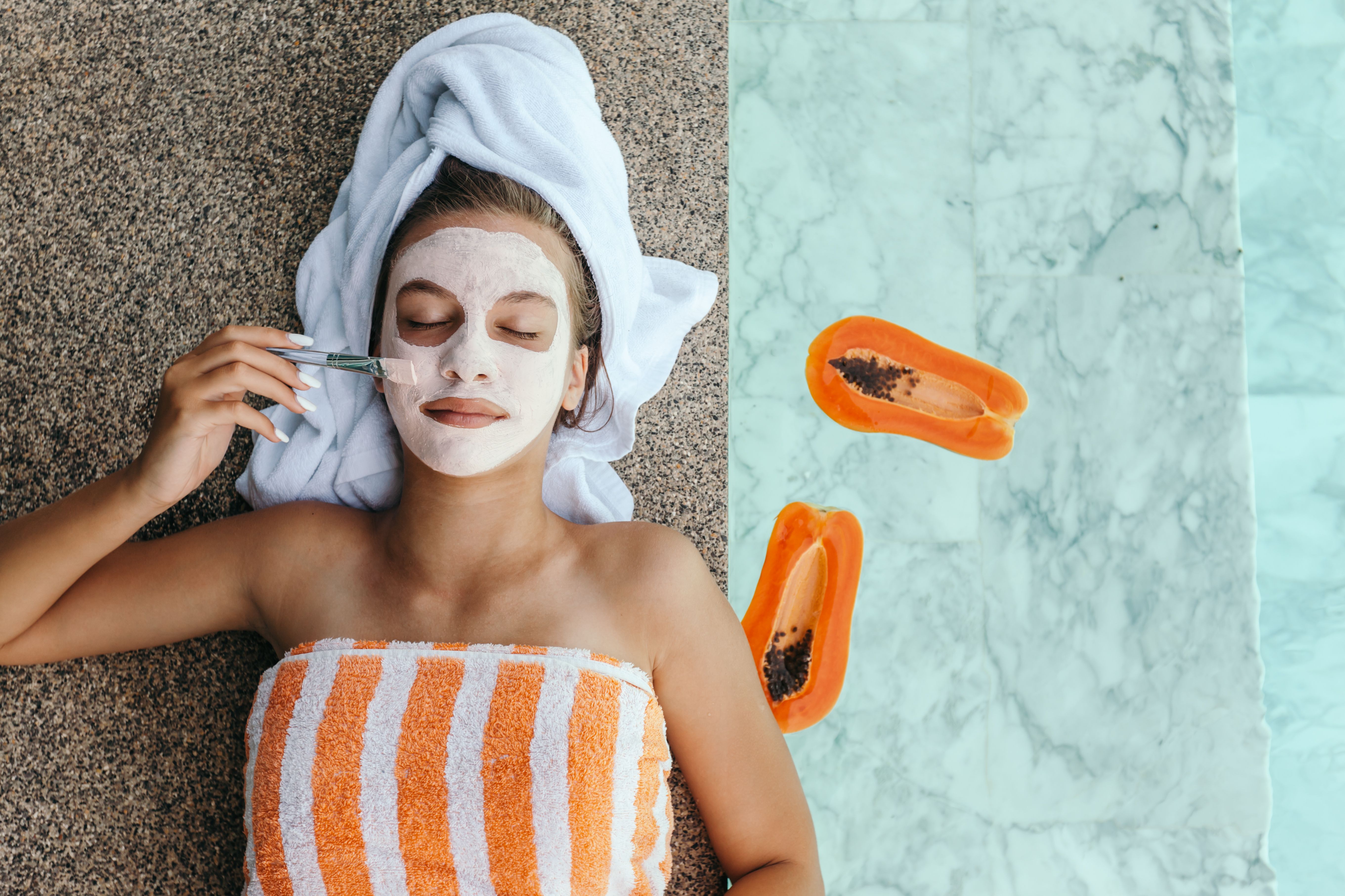 Woman wearing towels lounges poolside while applying a papaya face mask.