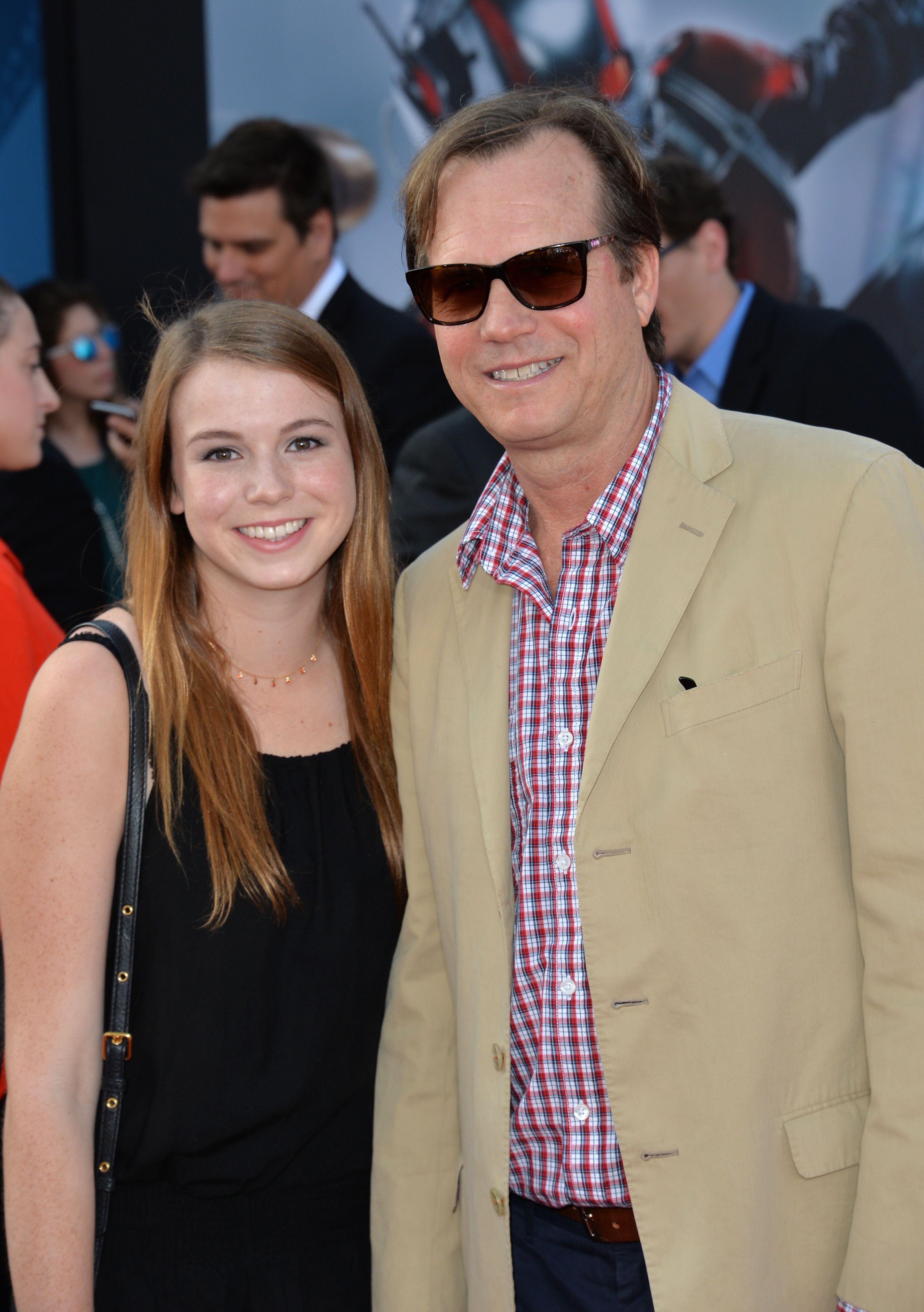 Lydia Paxton smiles in a black dress next to Bill in sunglasses and a tan blazer.