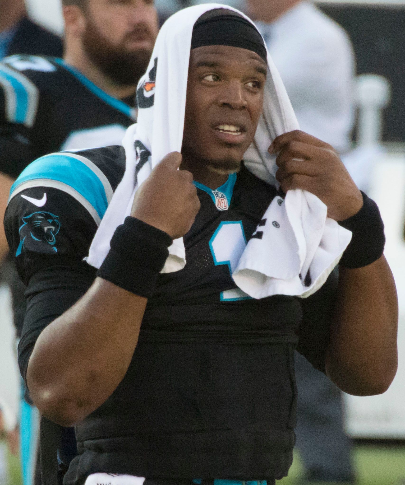 Cam Newton stands on the sidelines with a towel over his head.