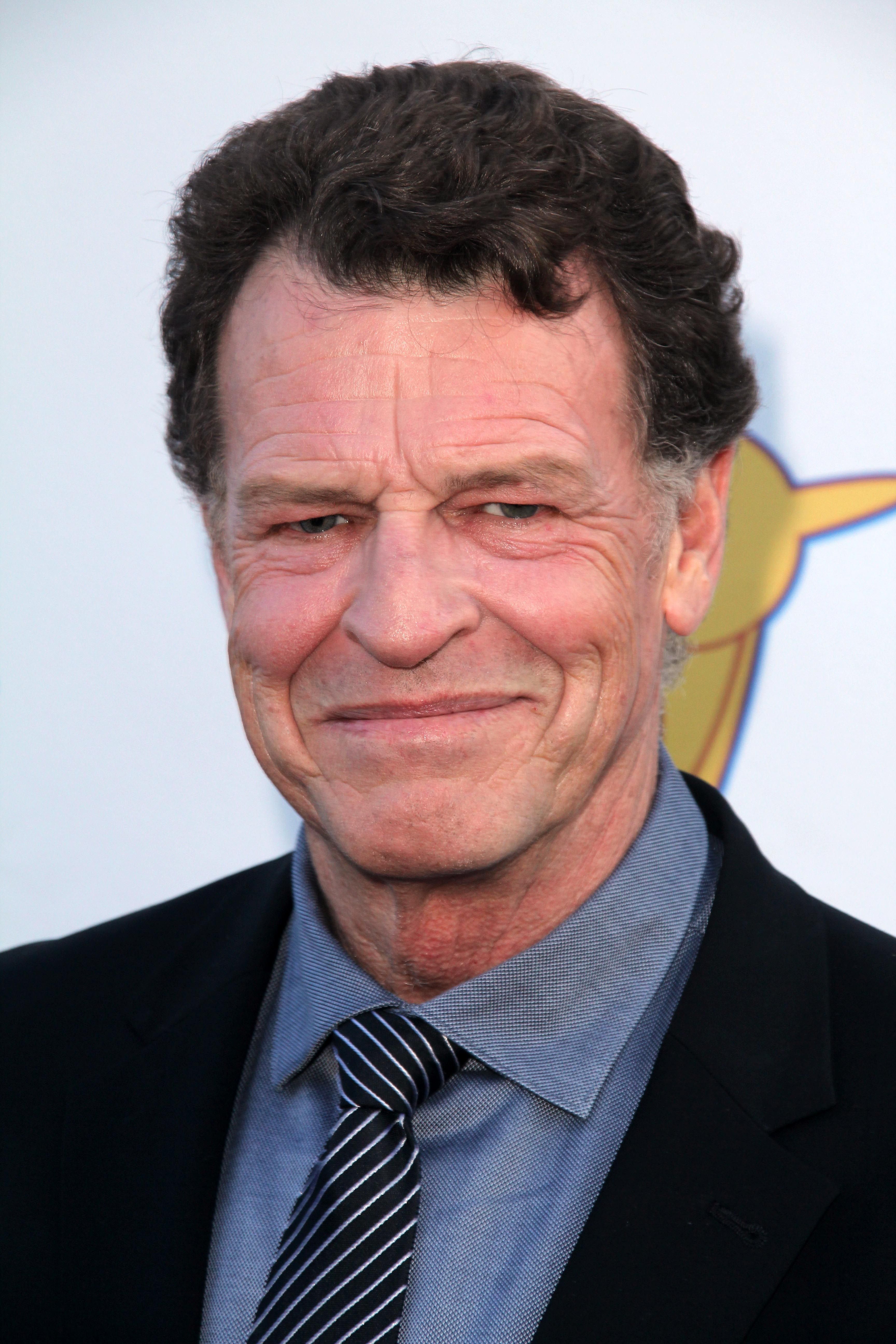 John Noble  wears a striped tie and blue shirt.