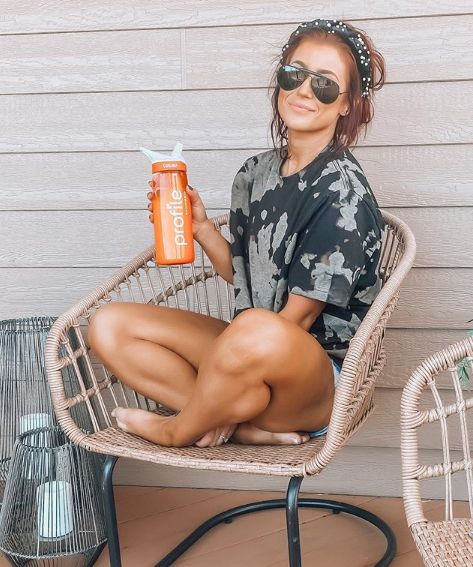 Chelsea Horca poses smiling on a porch in shorts