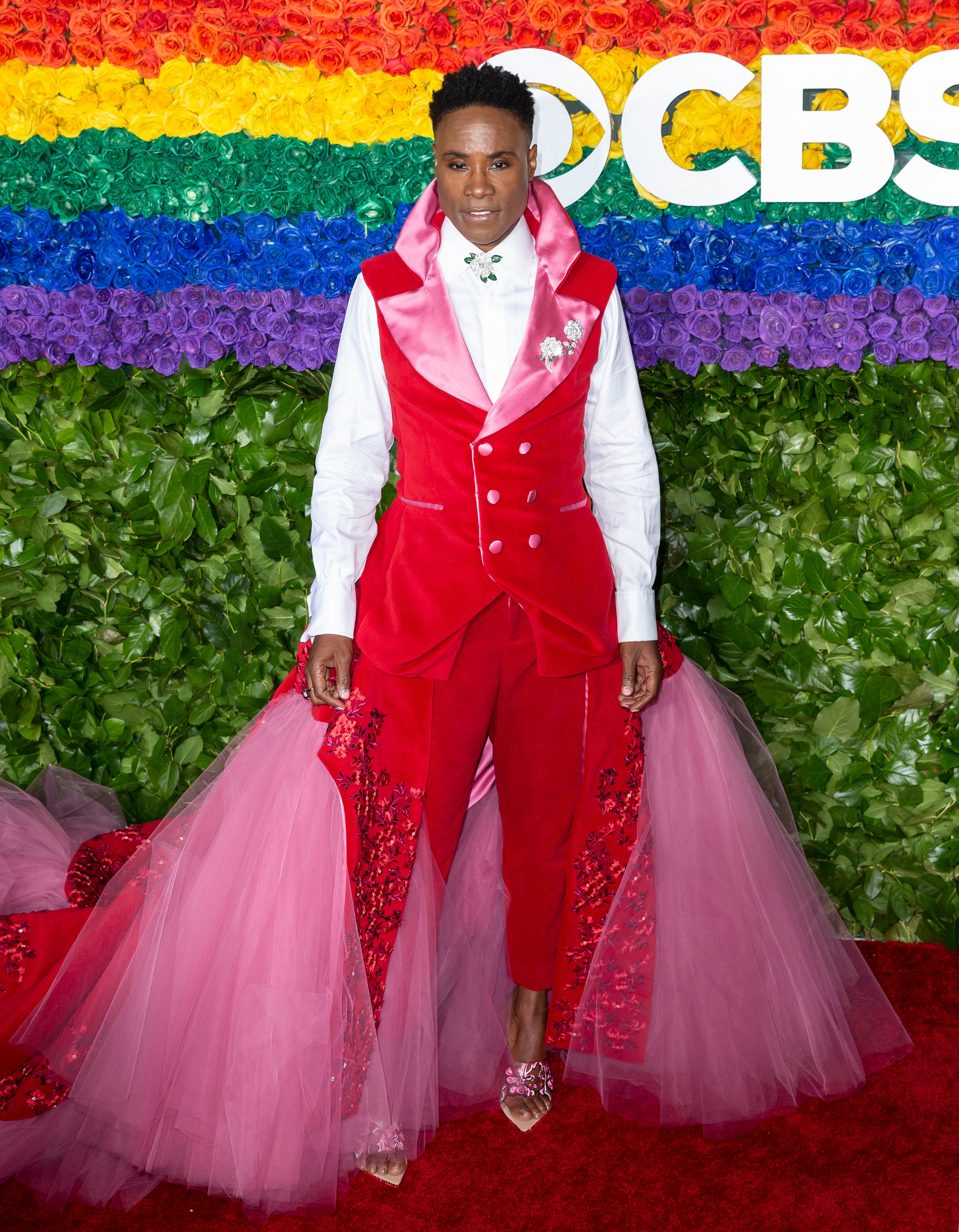 Billie Porter wears a red vest with a pink tulle skirt and heels.