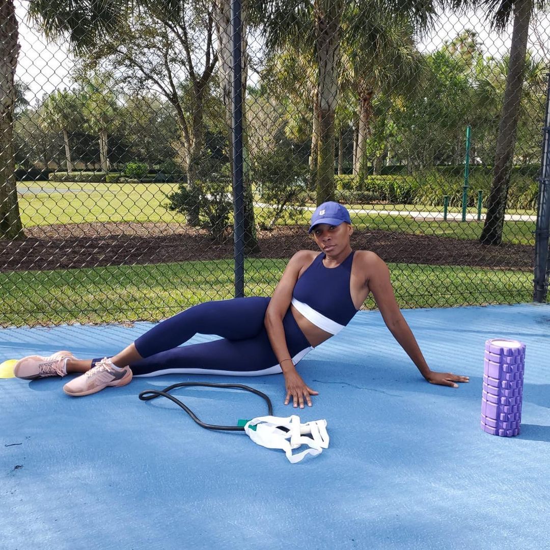 Venus Williams lounges on the court next to her fitness gear. 