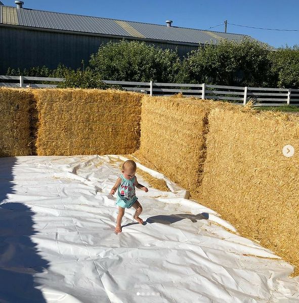 A toddler walking along the base tarp of a hay bale pool
