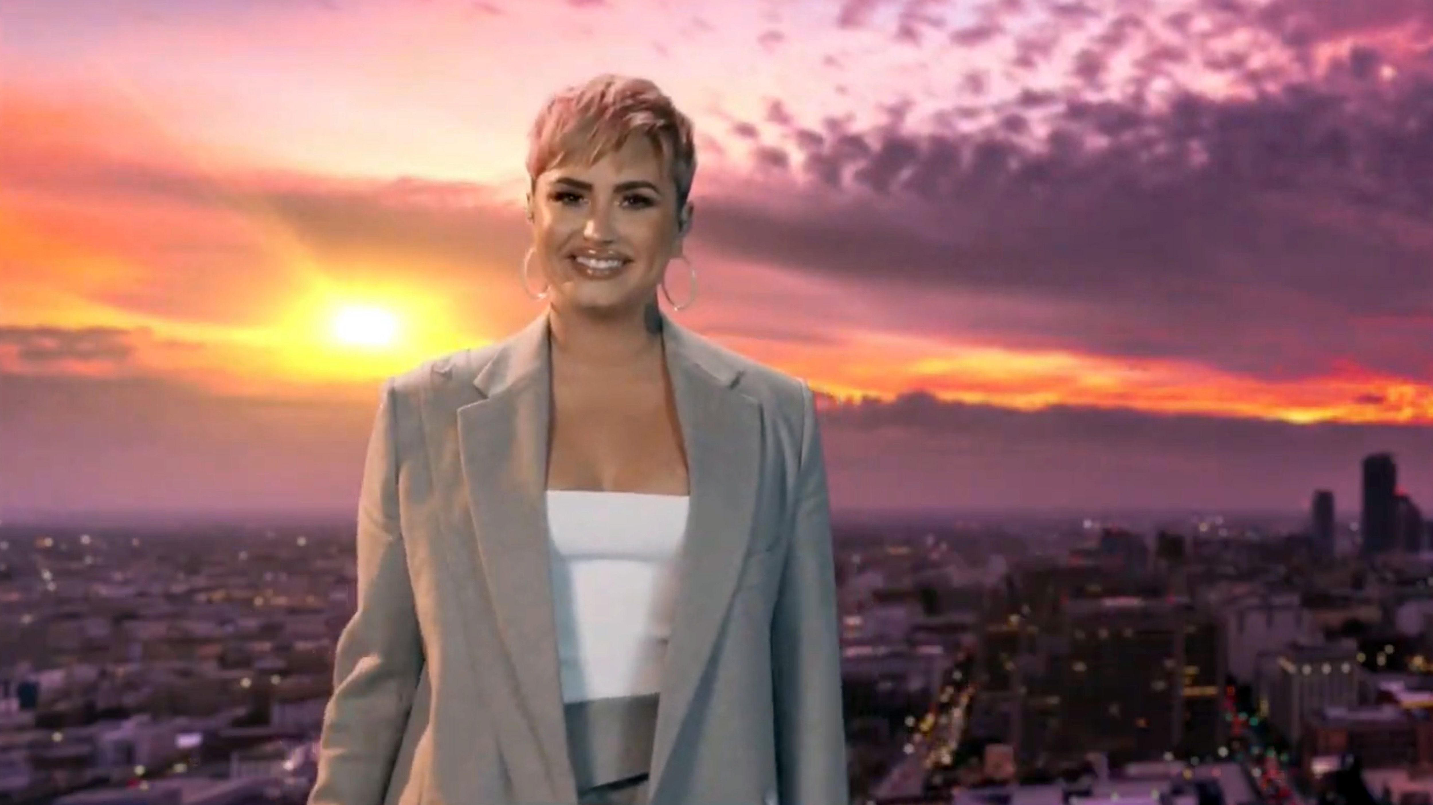 Demi Lovato wears a white shirt and gray blazer.