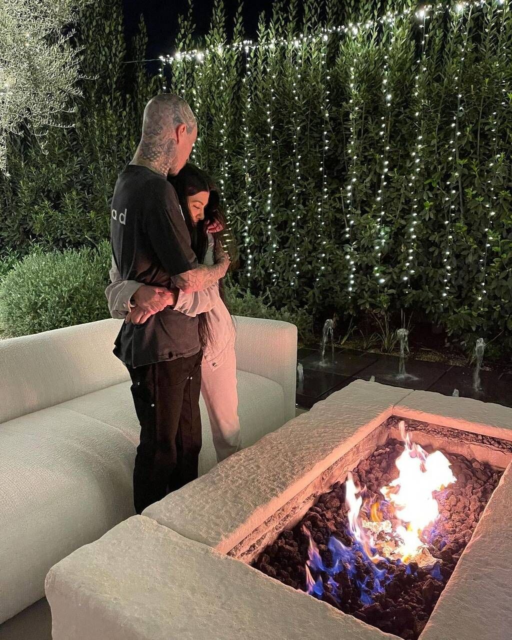 Travis Barker and Kourtney Kardashian hug in front of a fireplace.