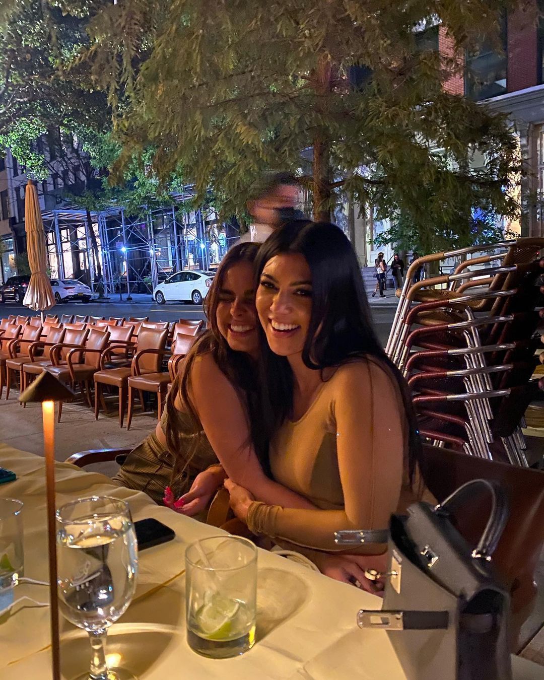 Addison Rae and Kourtney Kardashian snuggle on a bar terrace.
