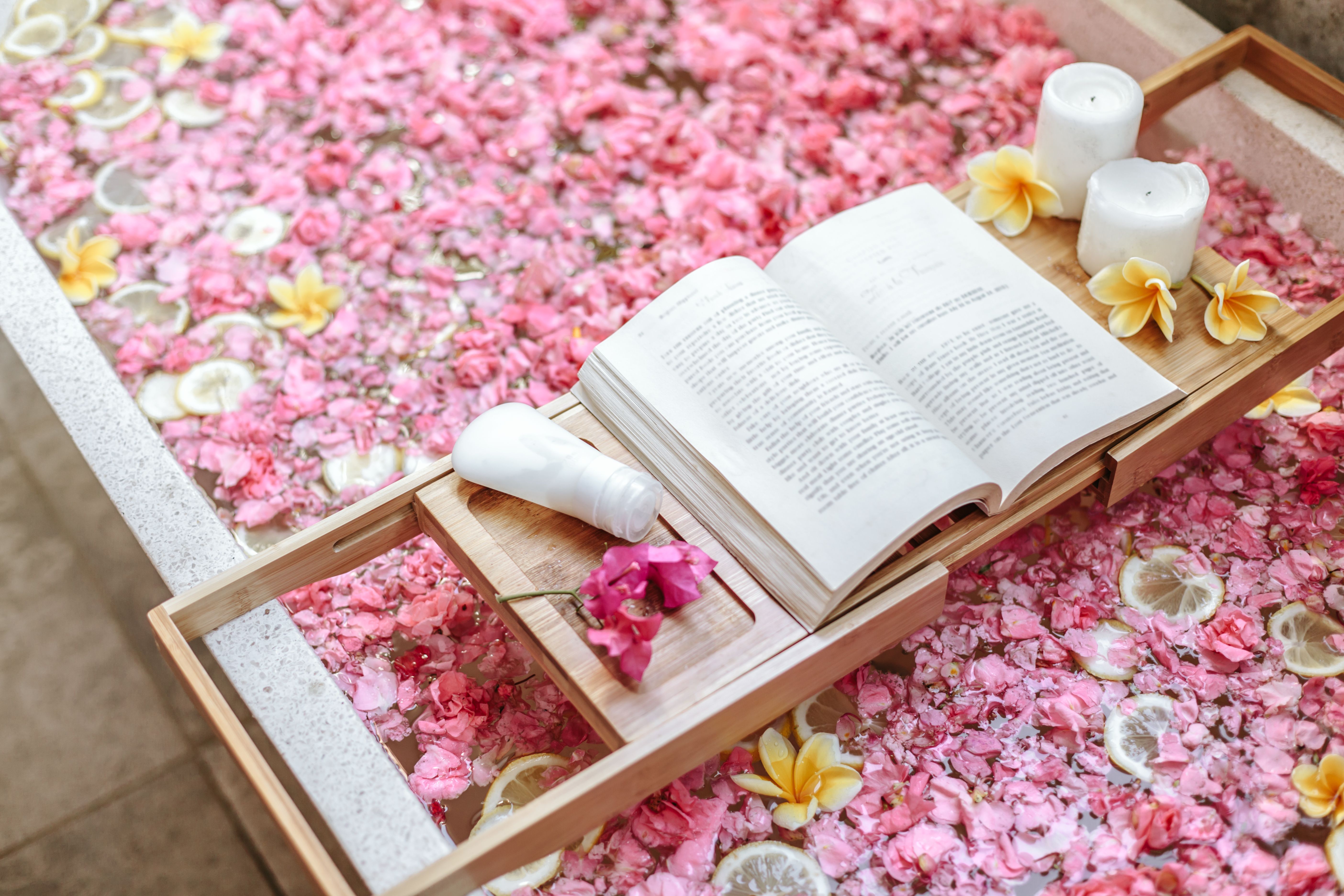 Tub filled with flower petals and a book stand with candles. 