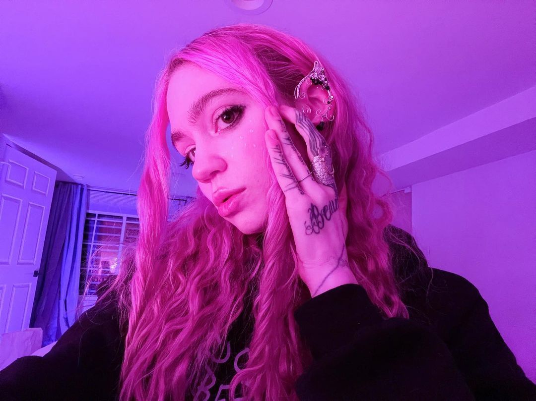 Grimes snaps a close-up selfie with black top and pink hair. 