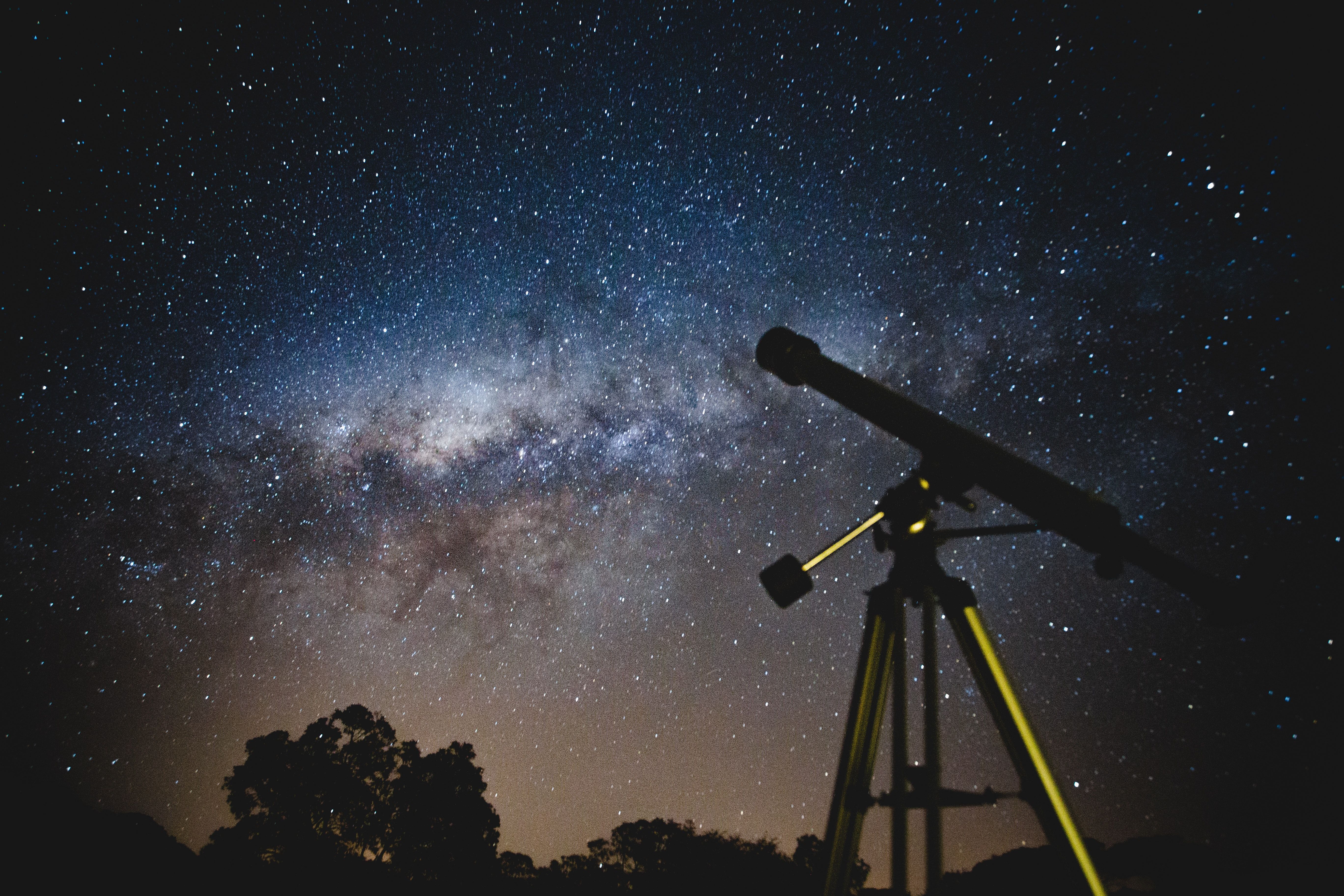A telescope points at the starry night sky and the Milky Way.