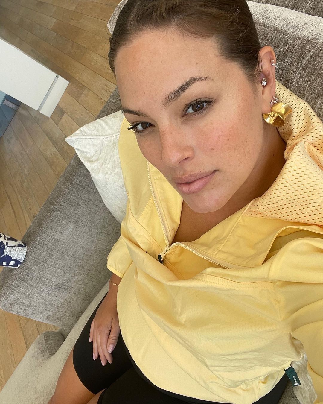 Ashley Graham takes a close-up snap in bicycle shorts and a yellow windbreaker.