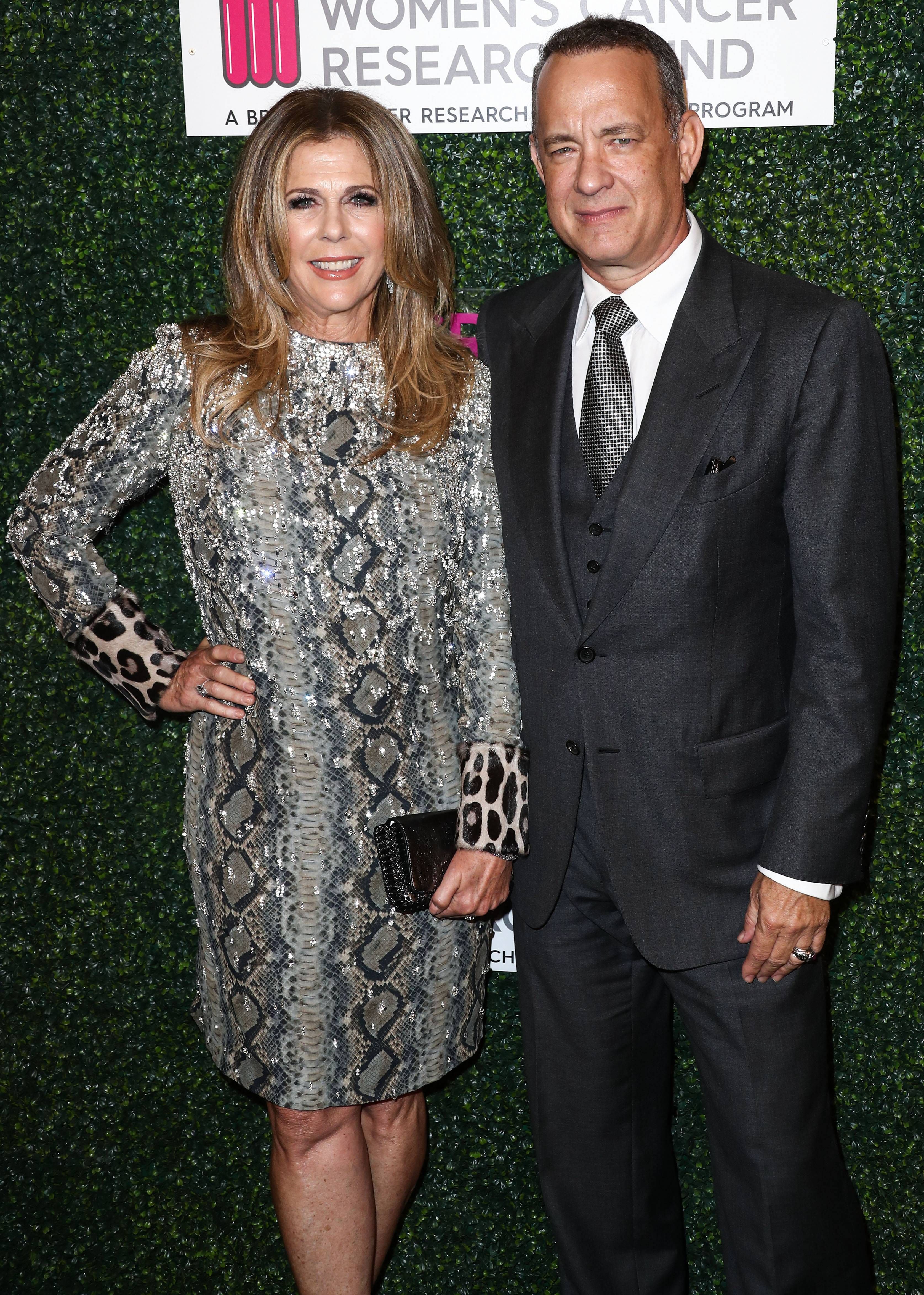 A lovely photo showing Riya Wilson in a snake-print knee-length dress, standing beside Tom Hanks, who has on a well-tailored black suit and pant, with dotted black tie to match.