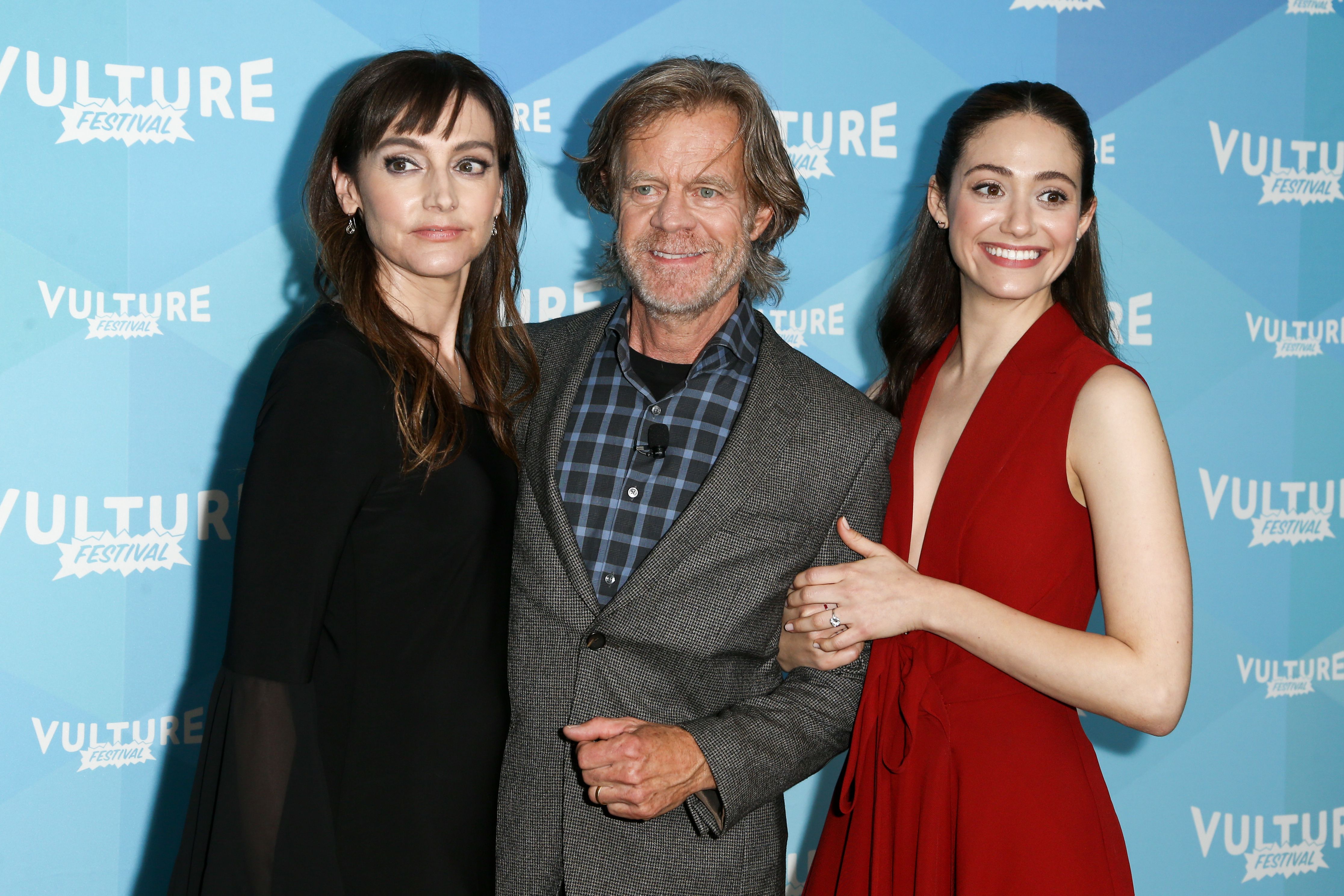 Wiliam H. Macy and Emmy Rossum stand side-by-side before a blue backdrop.
