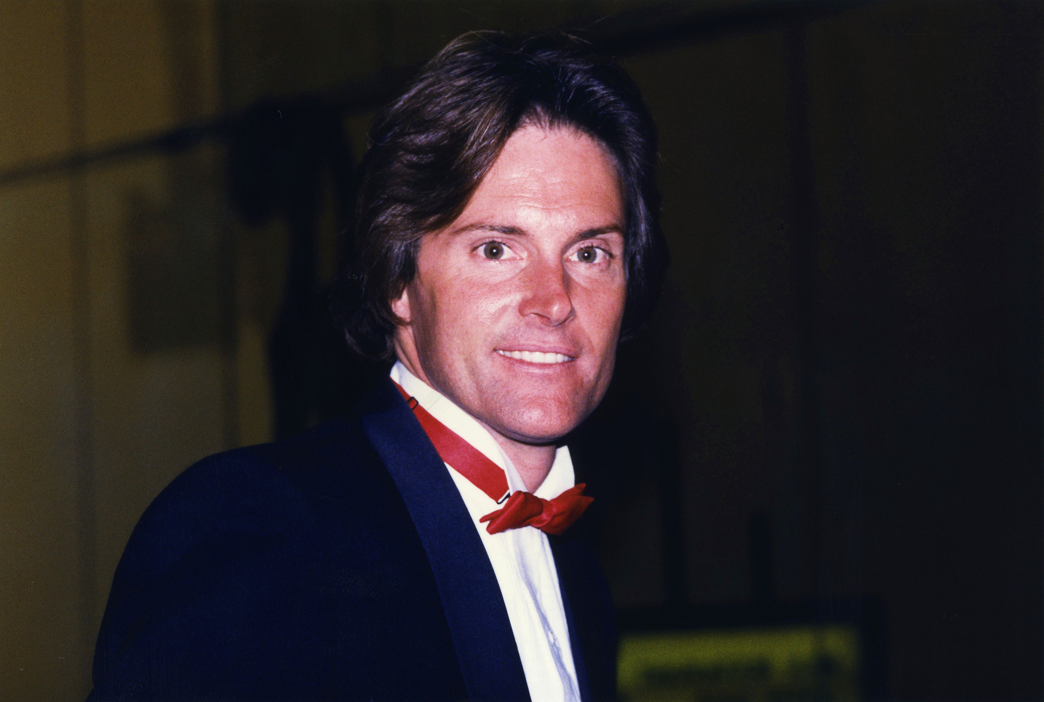 Bruce Jenner wears a red bow tie and suit.