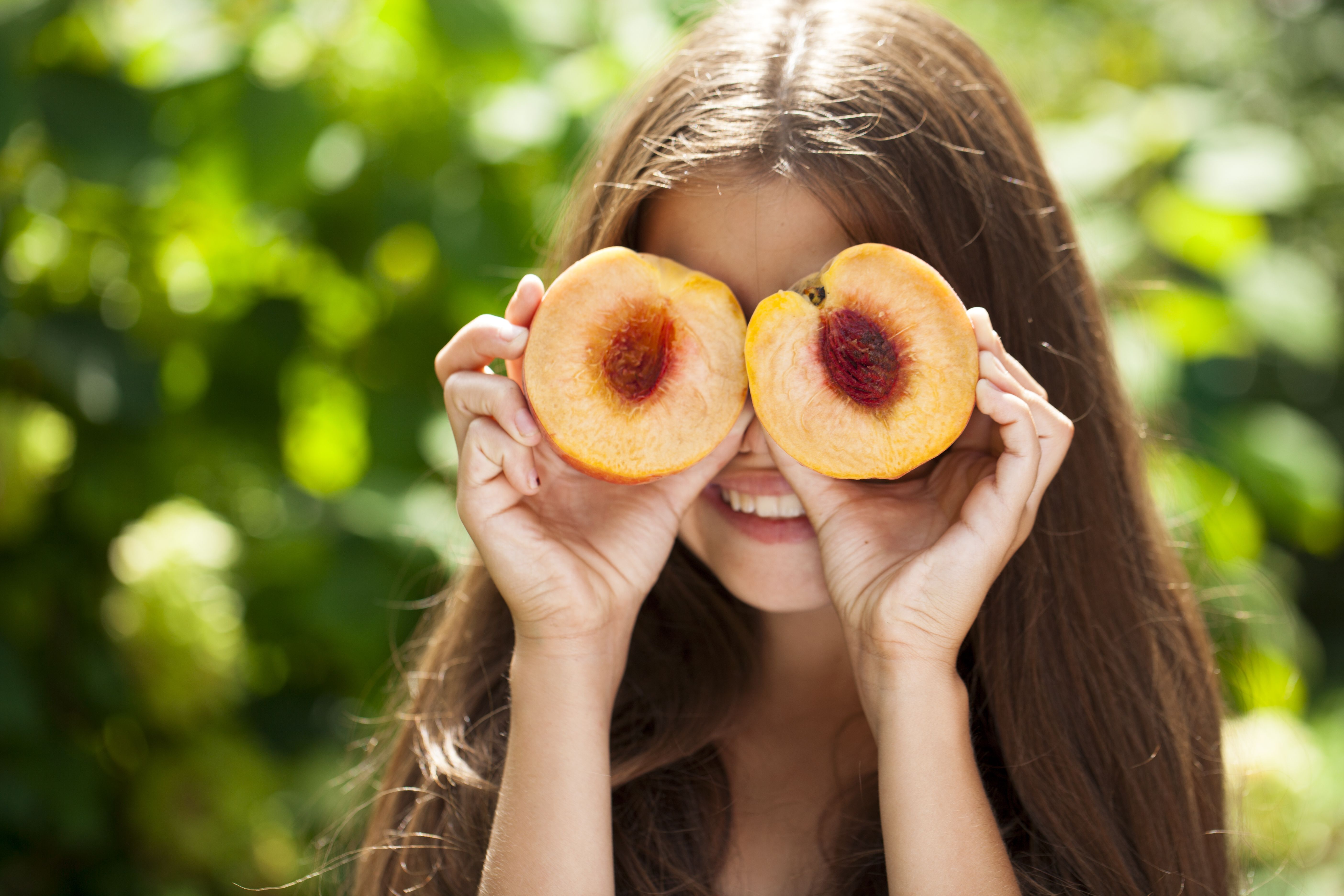 Woman holds up halved peaches in front of her eyes.