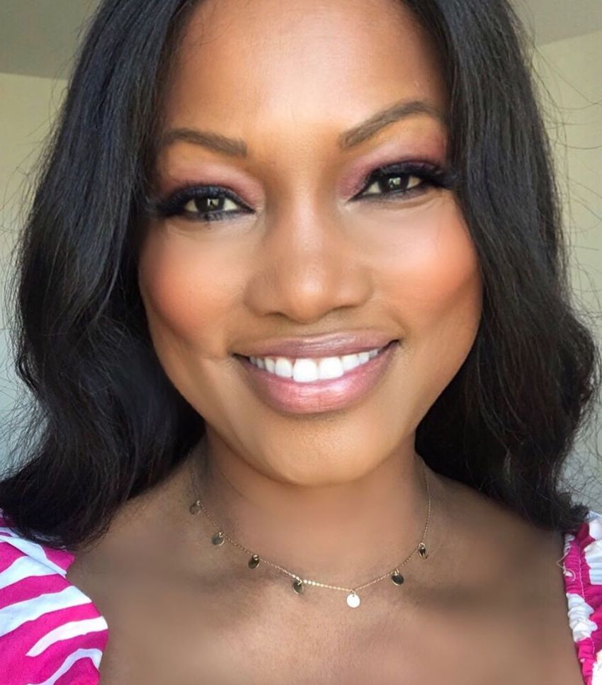 Garcelle Beauvais smiles in a pink and white shirt.