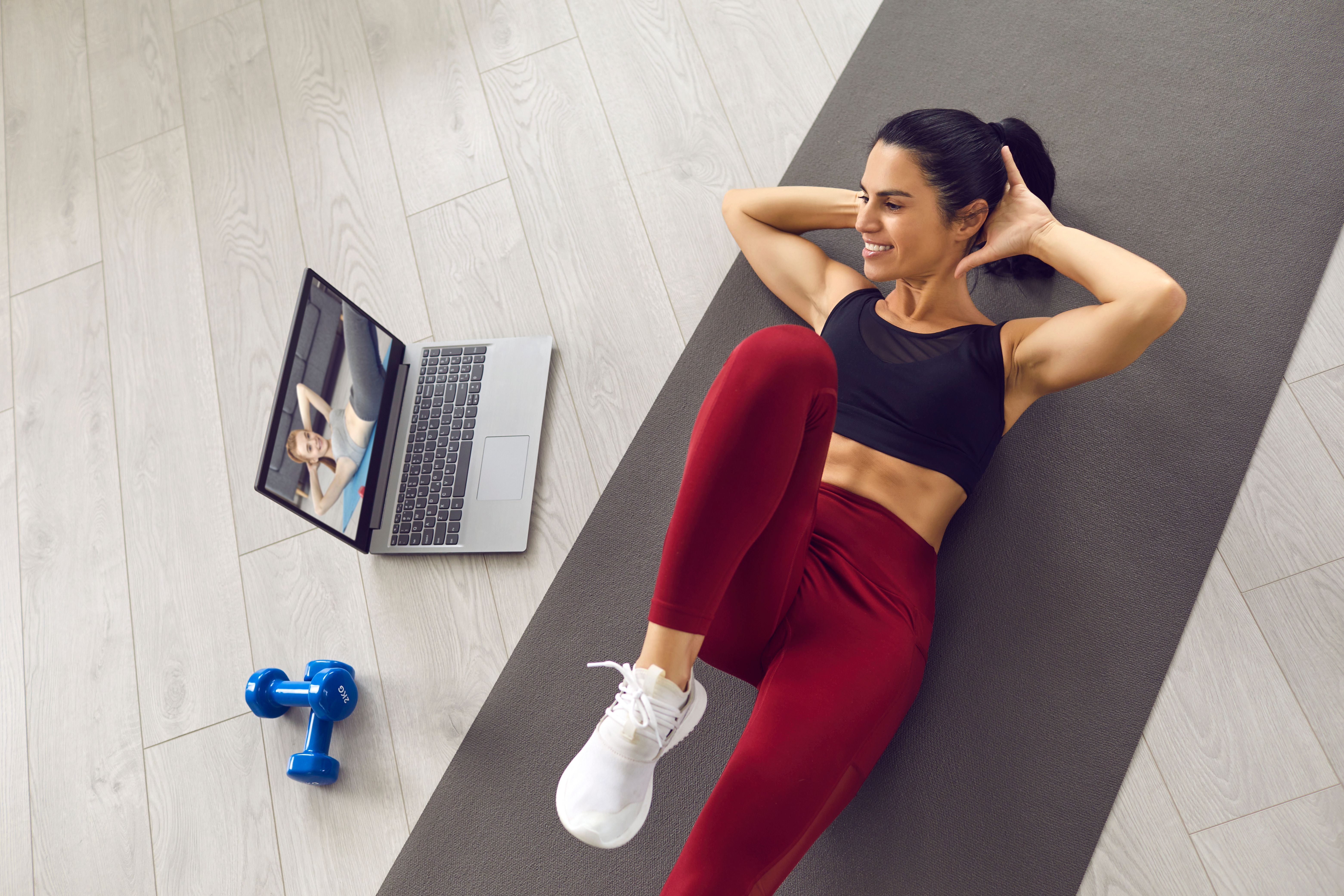 Young woman performs a core workout on exercise mat in front of open laptop. 