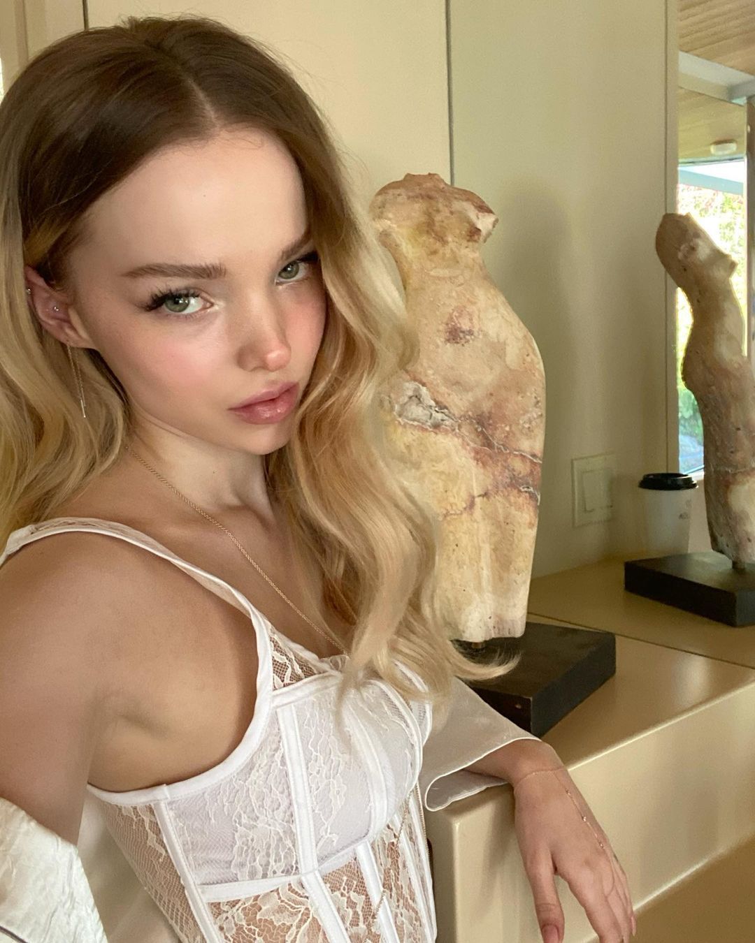 Dove Cameron rocks a white lace bustier in front of a statue.