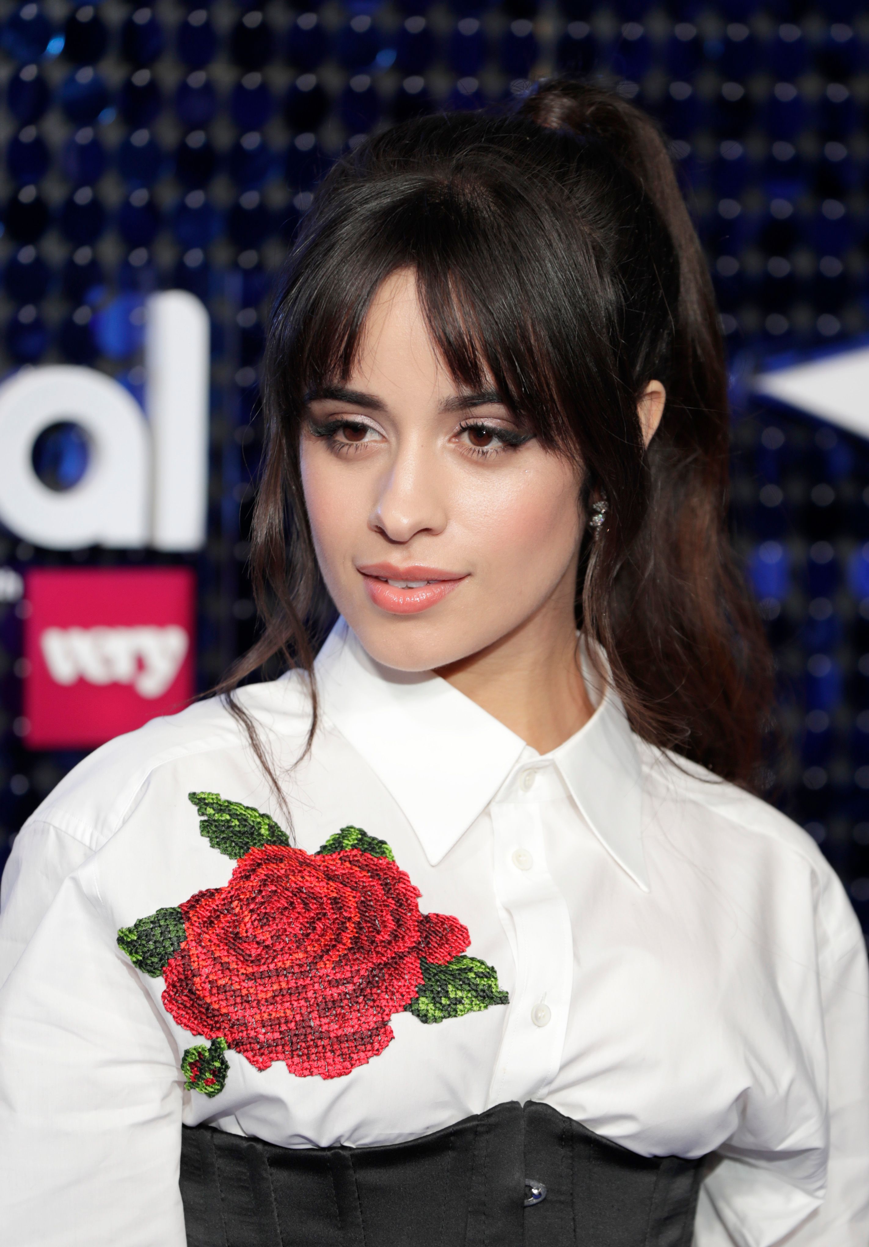 Camila Cabello wears a white button up with black corset and red rose.