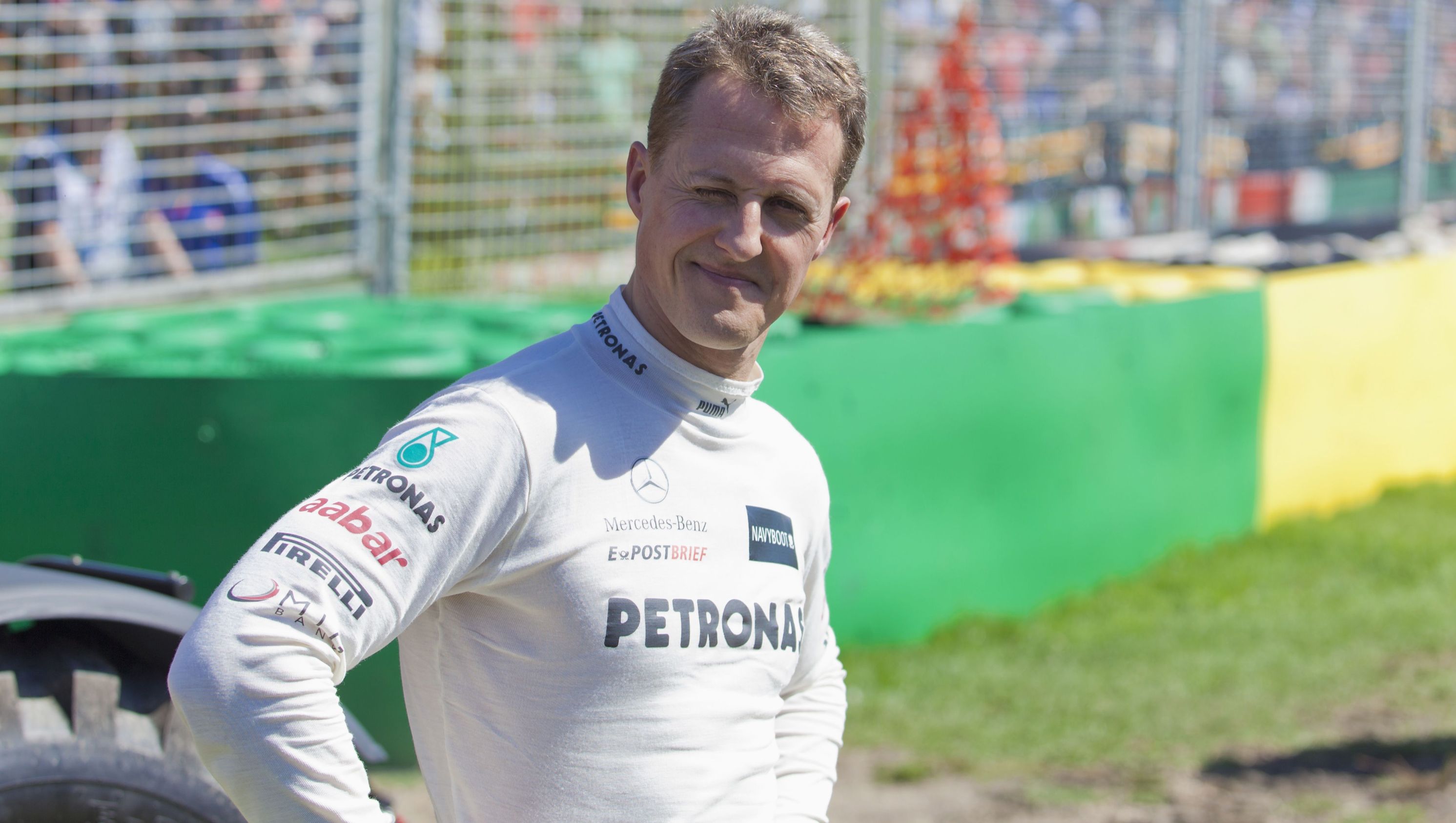 Michael Schumacher stands with hands on hips in white shirt.