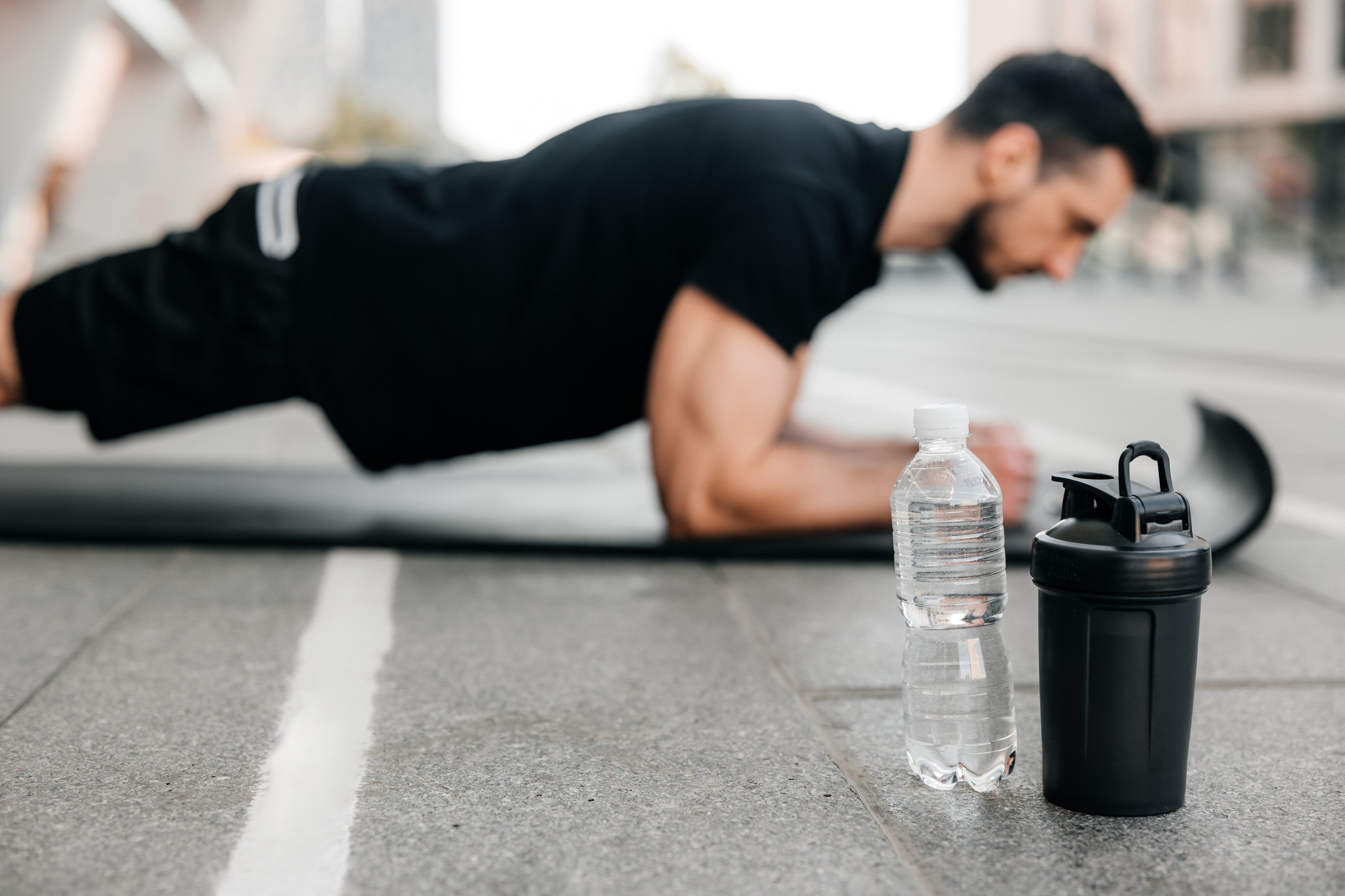 Young man doing planks on the sidewalk next to a water bottle. 