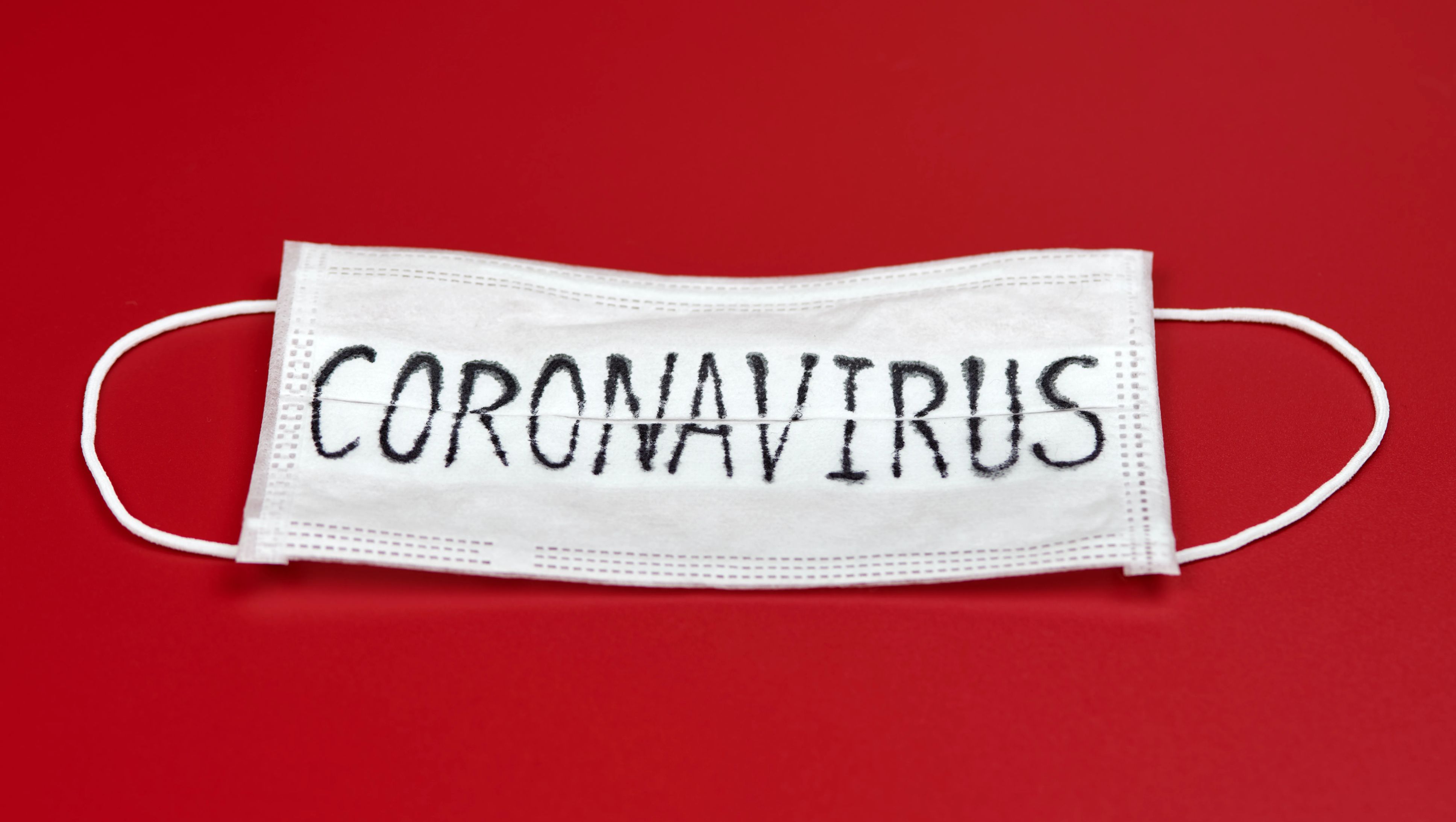 Surgical mask with the word 'coronavirus' written across, on red backdrop. 