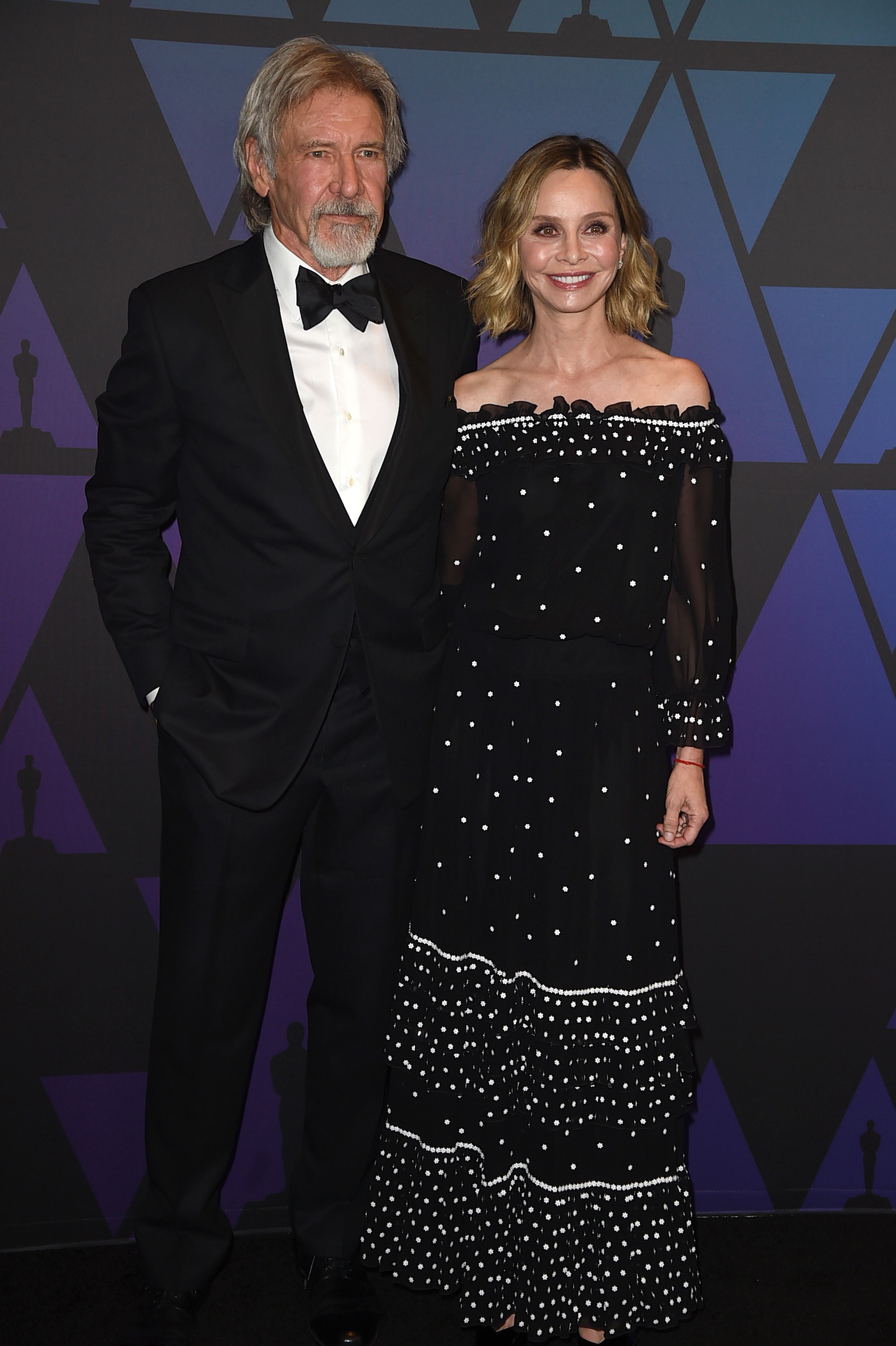 Harrison Ford stands beside wife Calista Flockhart in a black and white polka dot dress.
