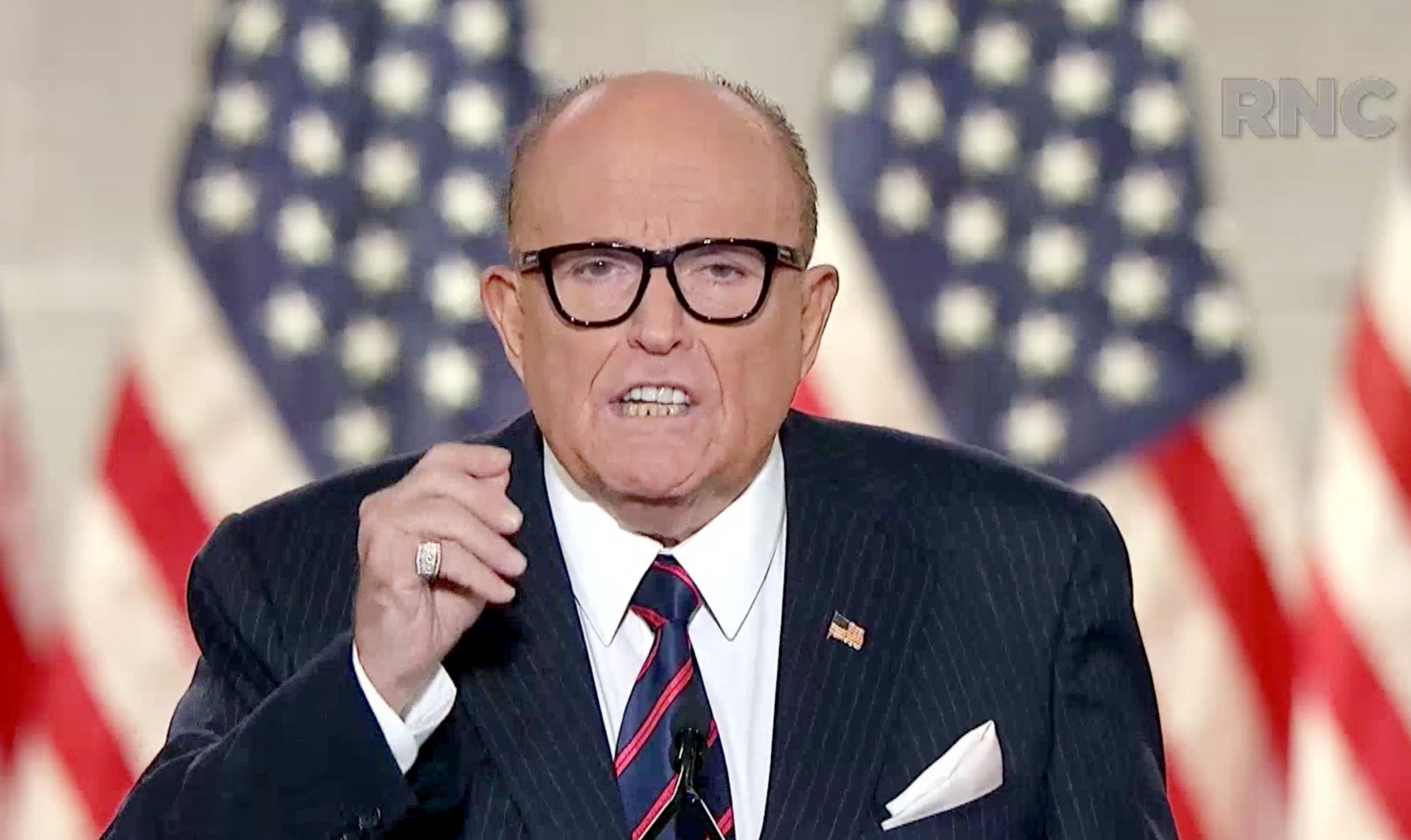 Rudy Giuliani in front of American flags.