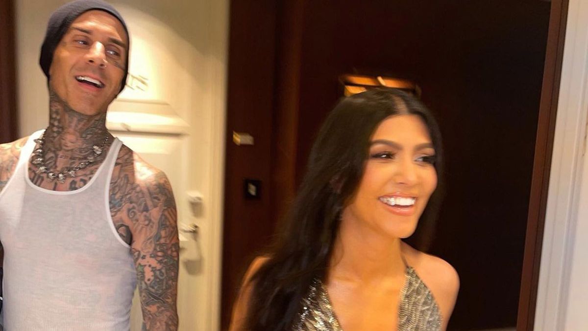 Travis Barker smiles in a white tank top and hat with Kourtney Kardashian.