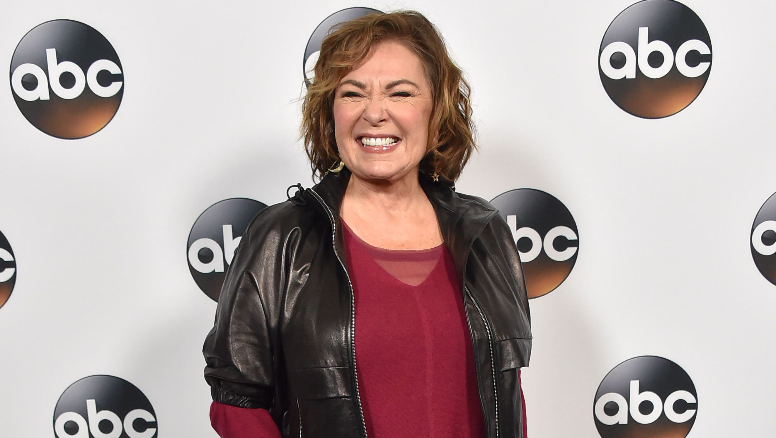 Roseanne Barr wears a red shirt and black jacket.