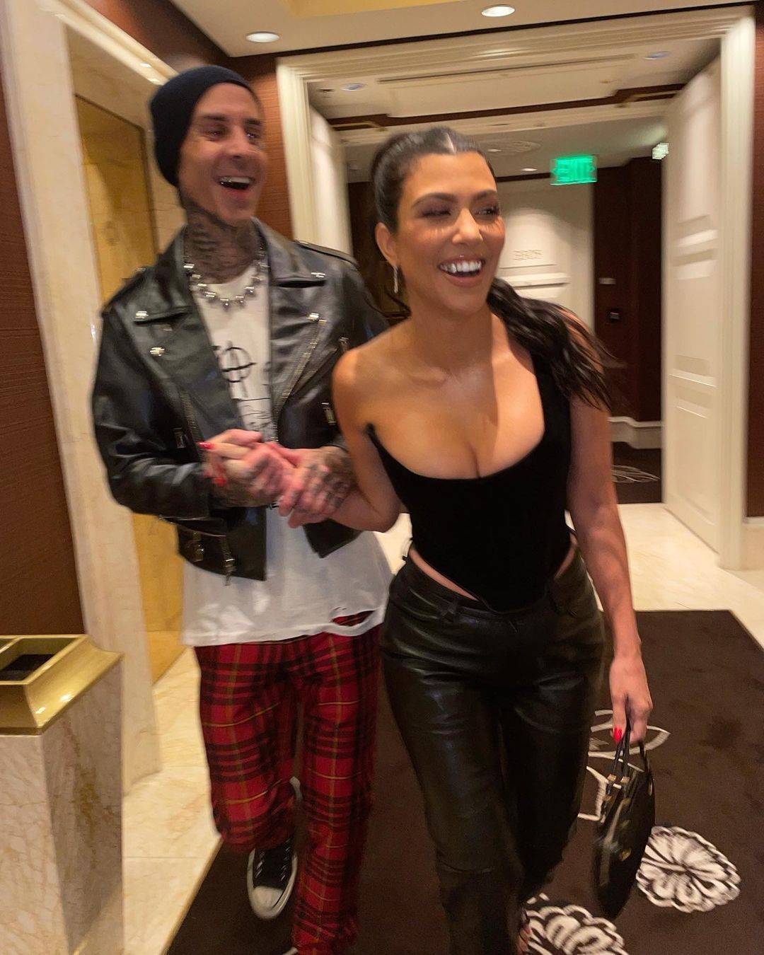 Travis Barker holds Kourtney Kardashian's hand while she walks in front of him.