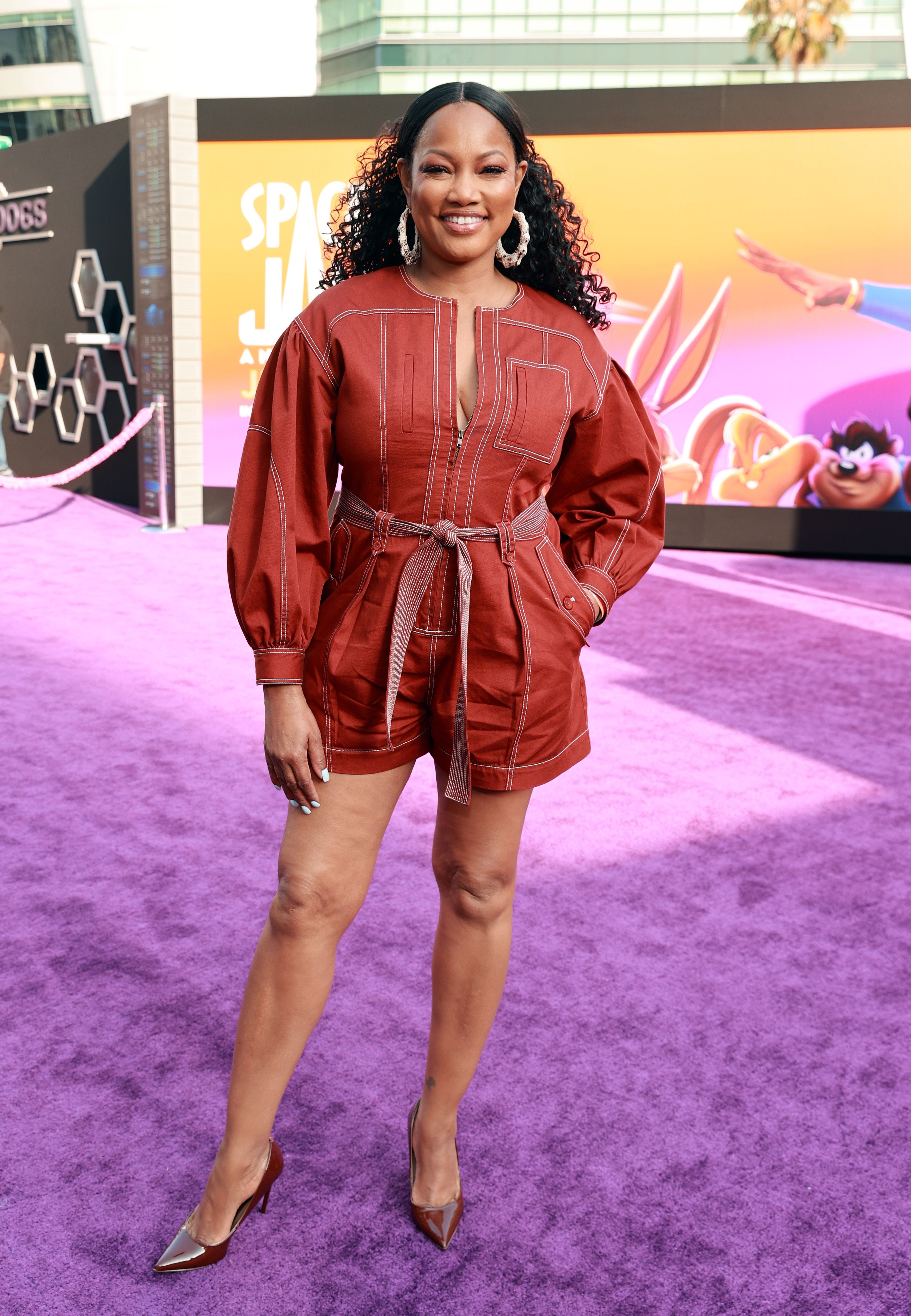 Garcelle Beauvais wears a red romper and gold hoop earrings.