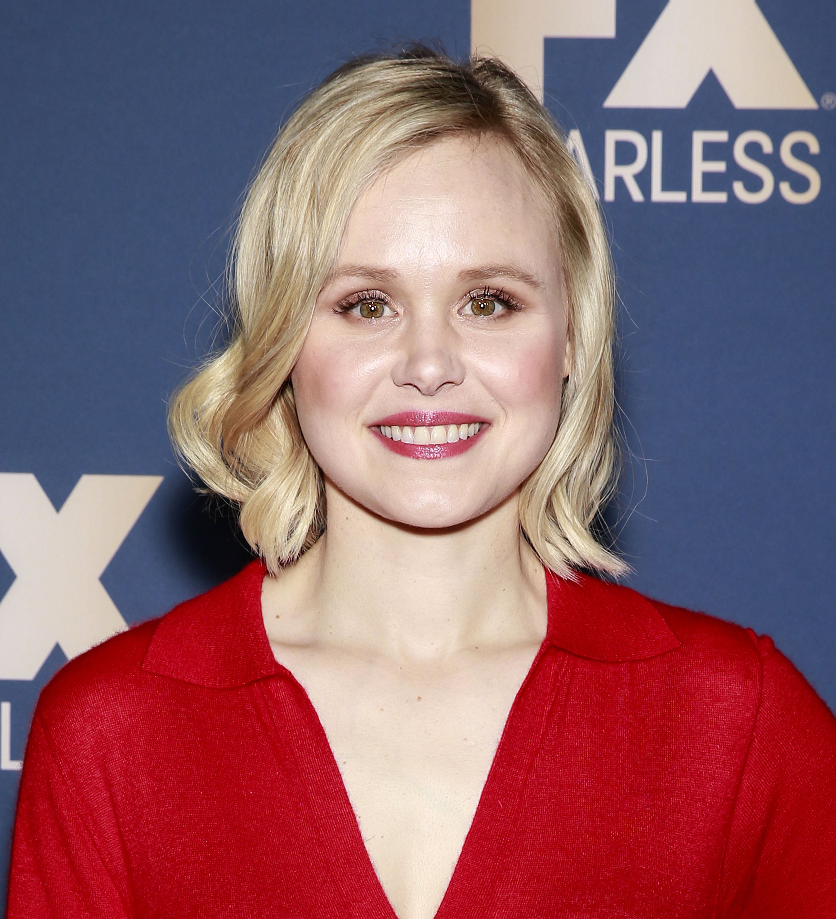Alison Pill wears red and red lipstick with curly hair.