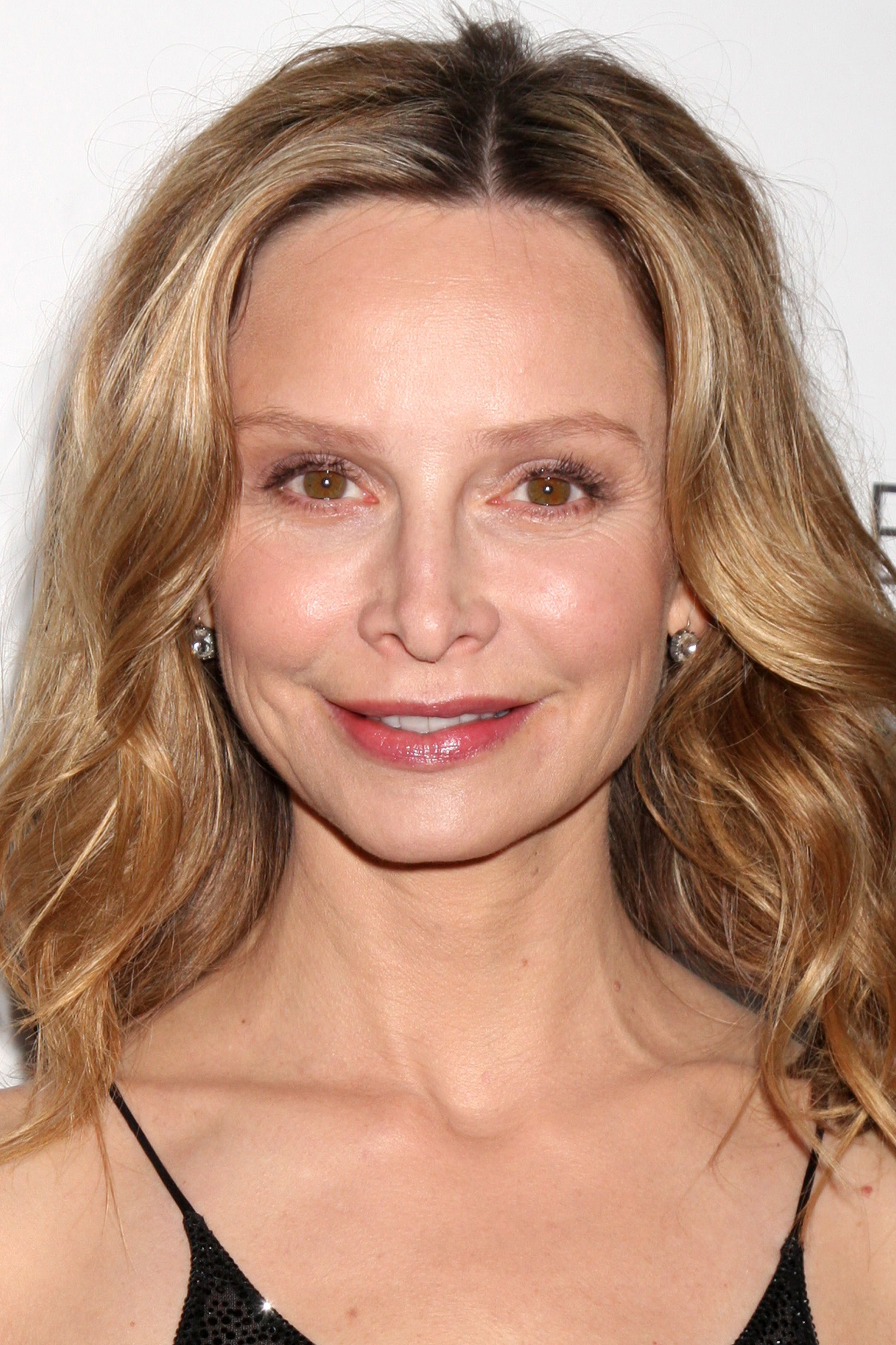 Calista Flockhart wears a black dress with diamond earrings and smiles.