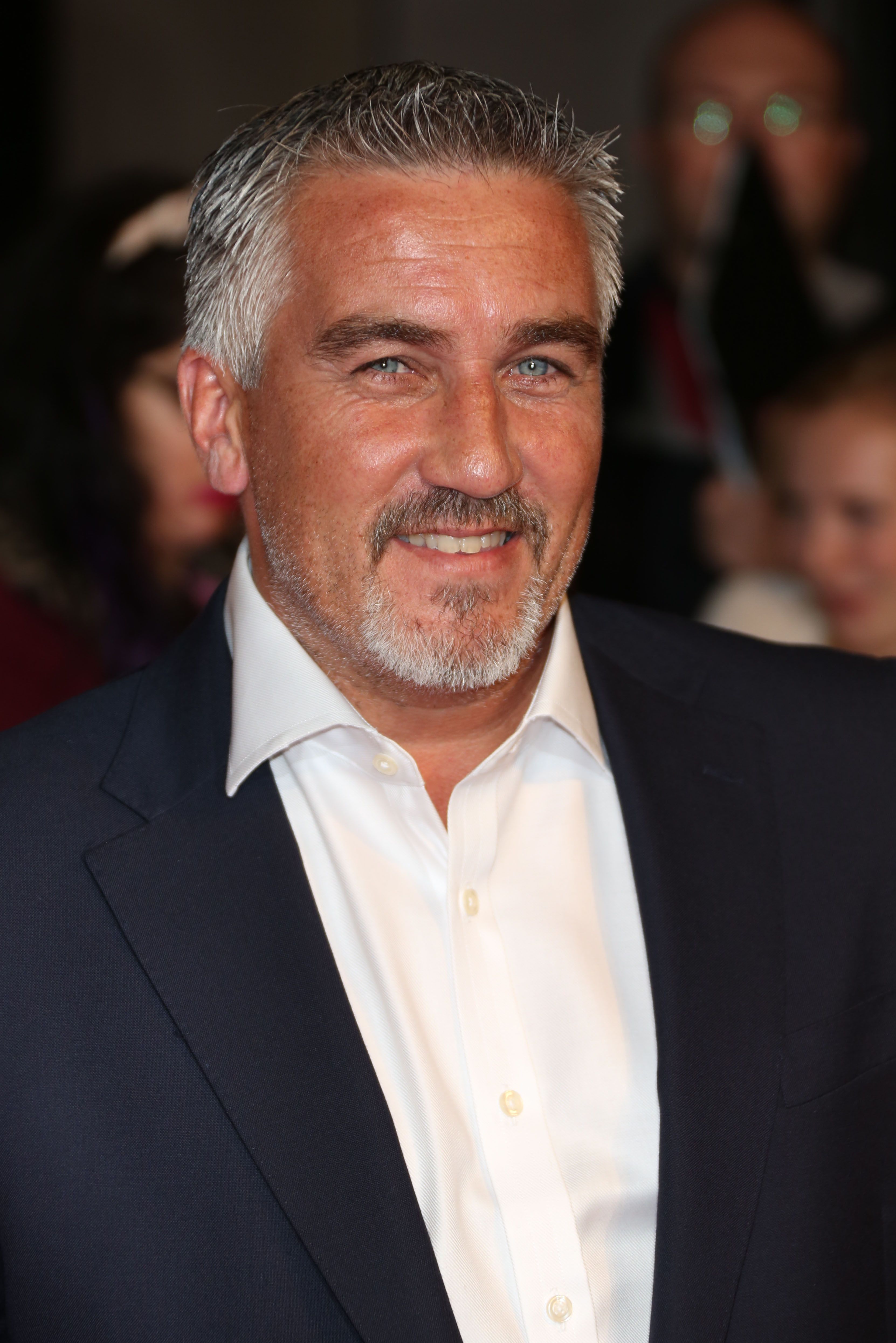 Paul Hollywood smiles in a navy blue suit.