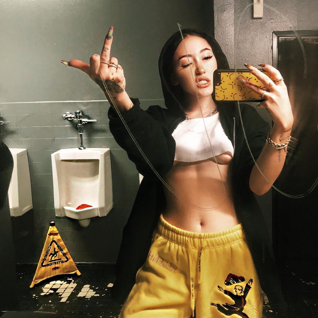 Noah Cyrus poses in front of a urinal in a crop top.